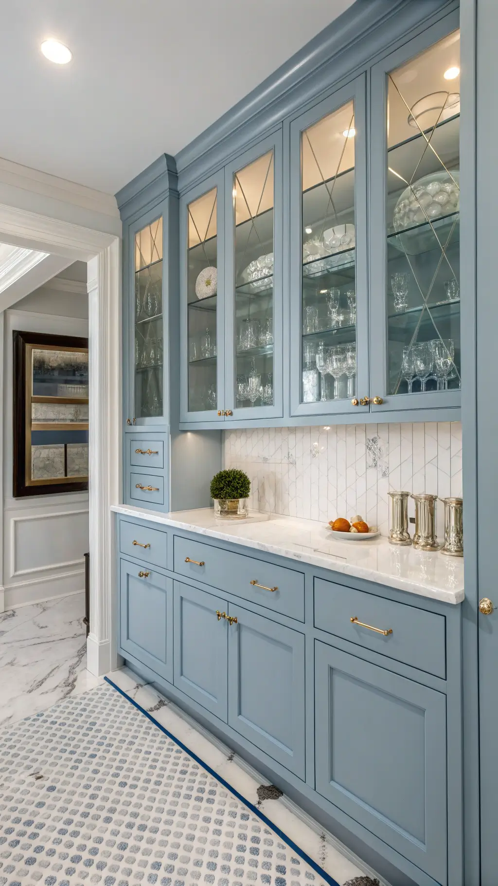 Powder blue butler's pantry with glass-front cabinets, white marble counters, mosaic floor tiles, and antique mirror backsplash reflecting natural light