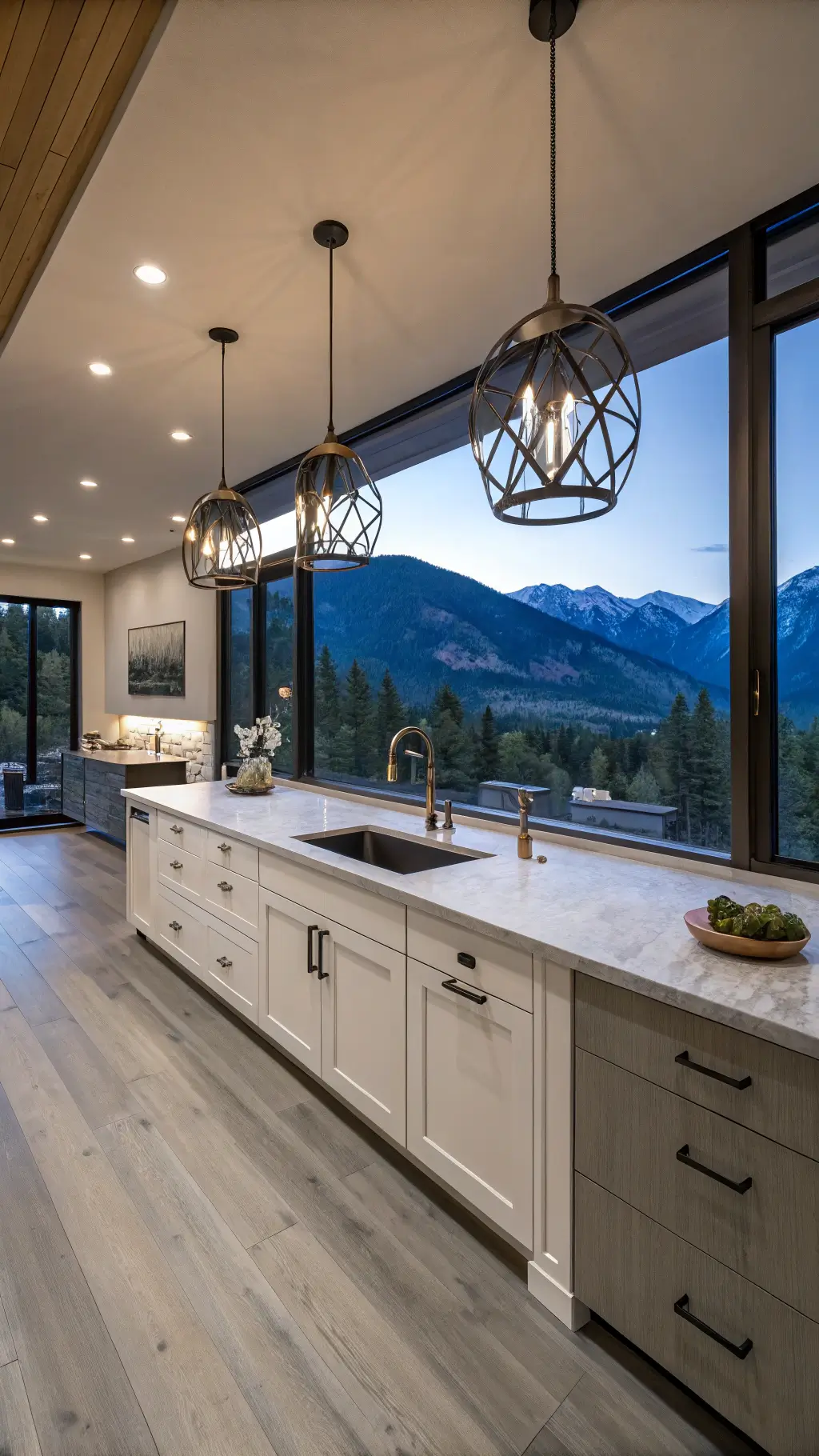 Evening view of a mountain-modern kitchen with white oak cabinets, leathered granite counters, mixed metal fixtures, and steel-framed windows overlooking mountains during blue hour