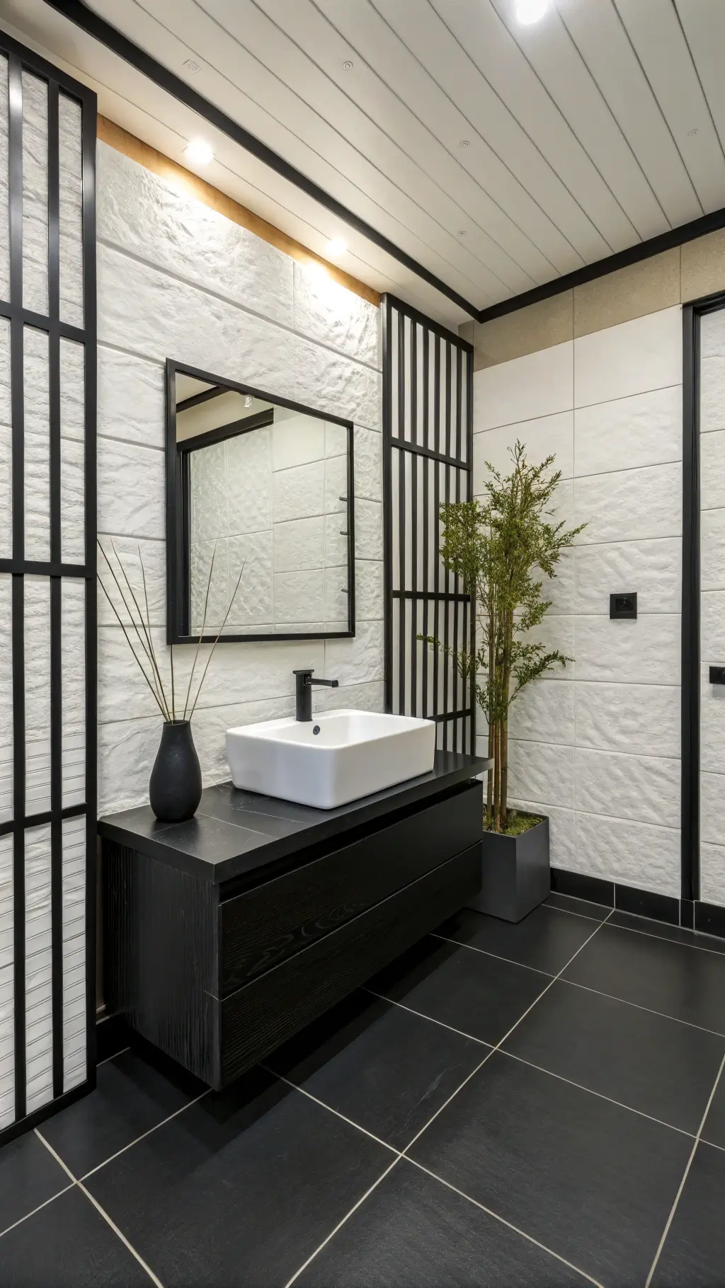 Minimalist Japanese-inspired bathroom with black vanity, white sink, textured wall panels, large black floor tiles, bamboo plant, and diffused overhead lighting